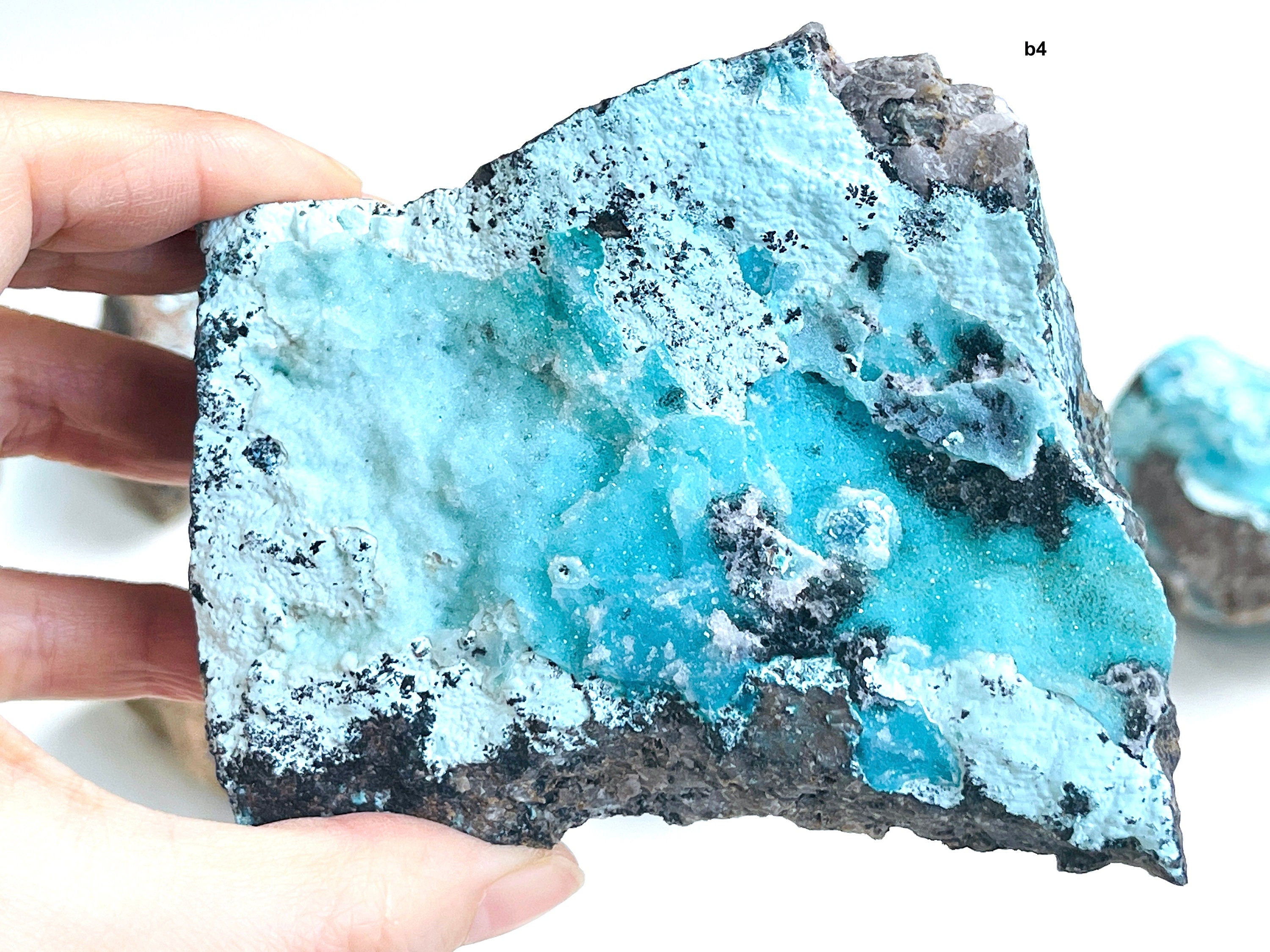 Turquoise blue chysocolla mineral specimen held by a hand on a white background