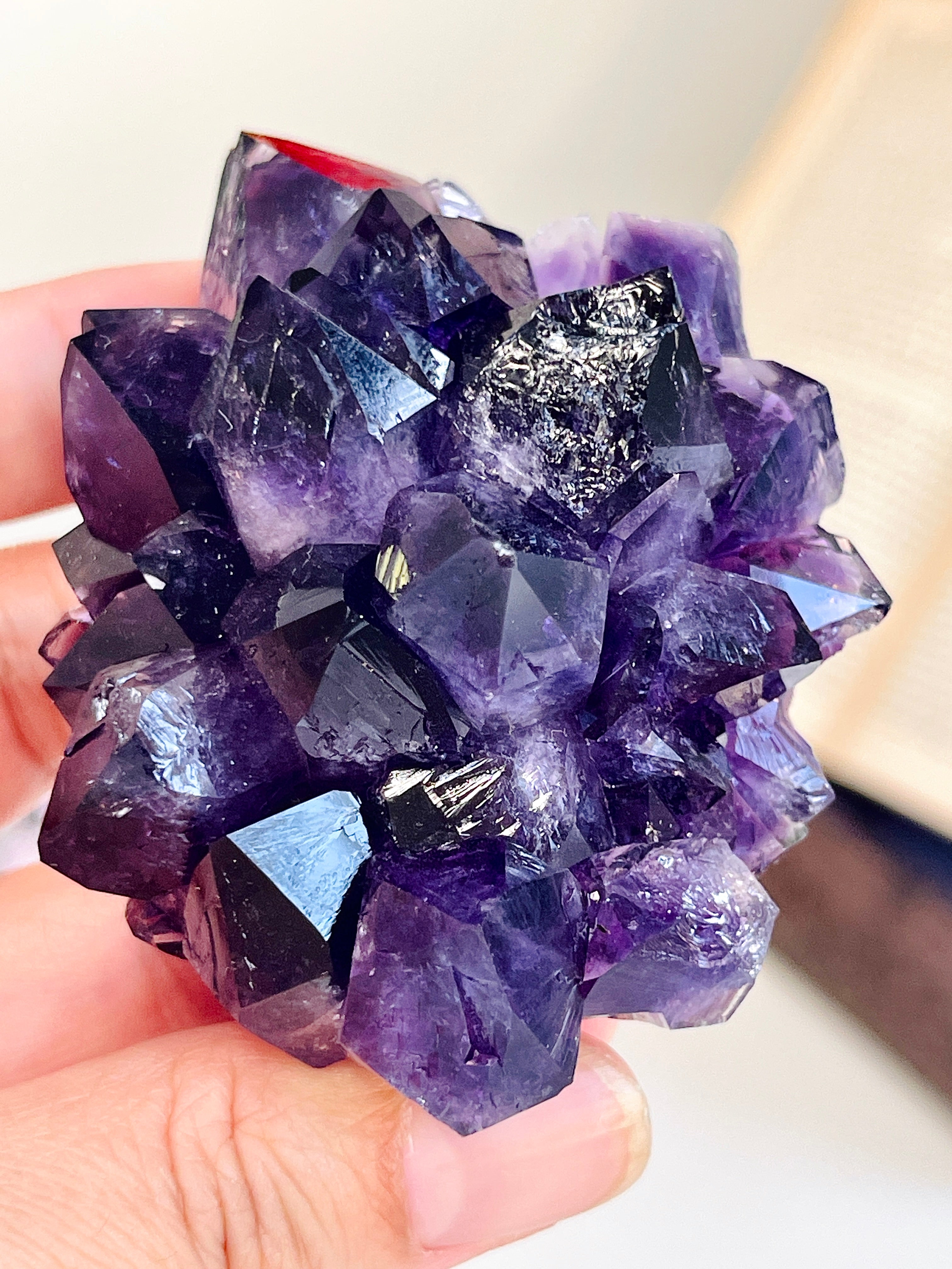 A hand holding a cluster of purple amethyst crystals with dark, faceted points against a softly blurred light background.