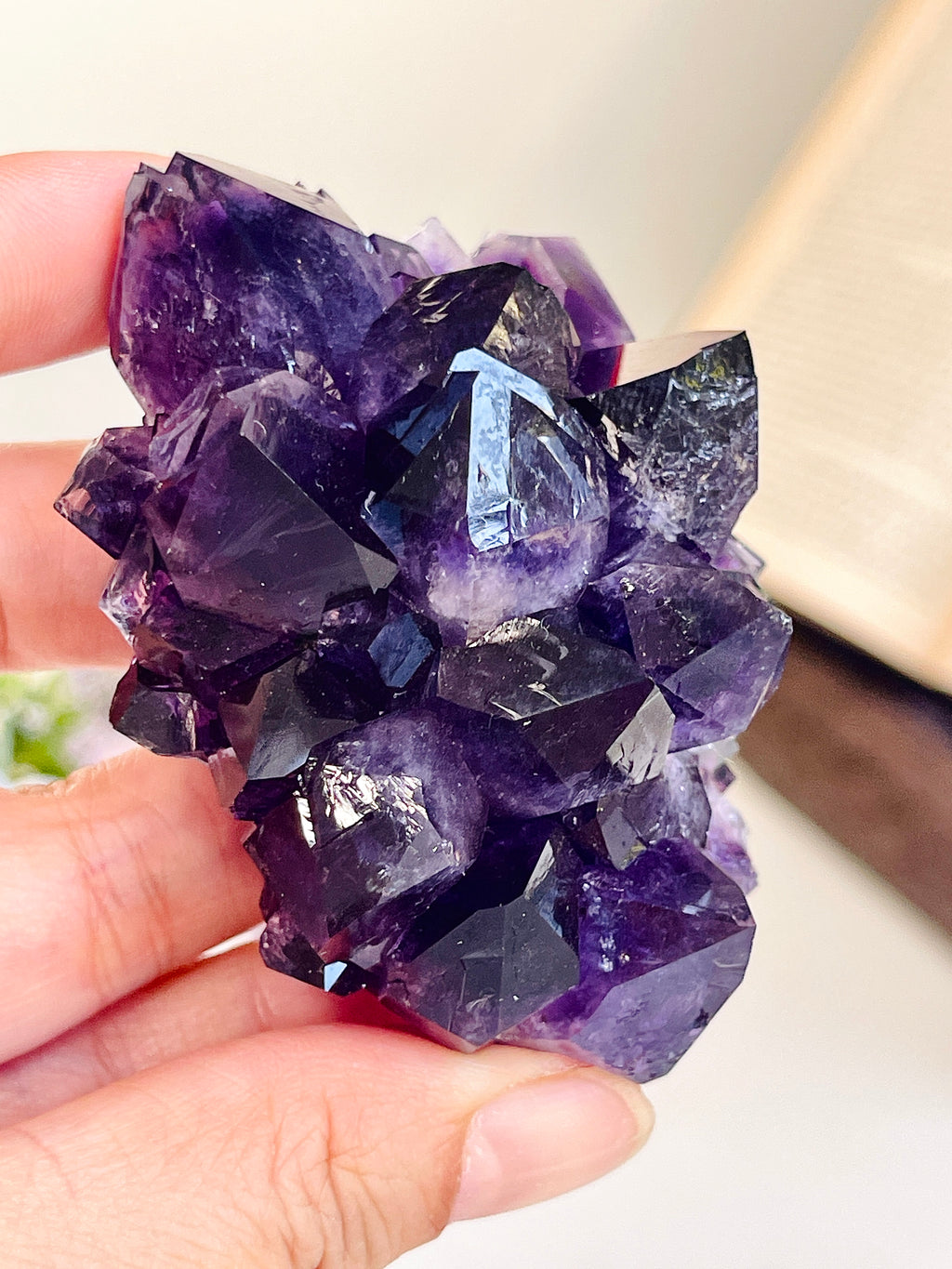 A hand holding a cluster of purple amethyst crystal points, showing the natural jagged facets and varying shades of translucent purple.