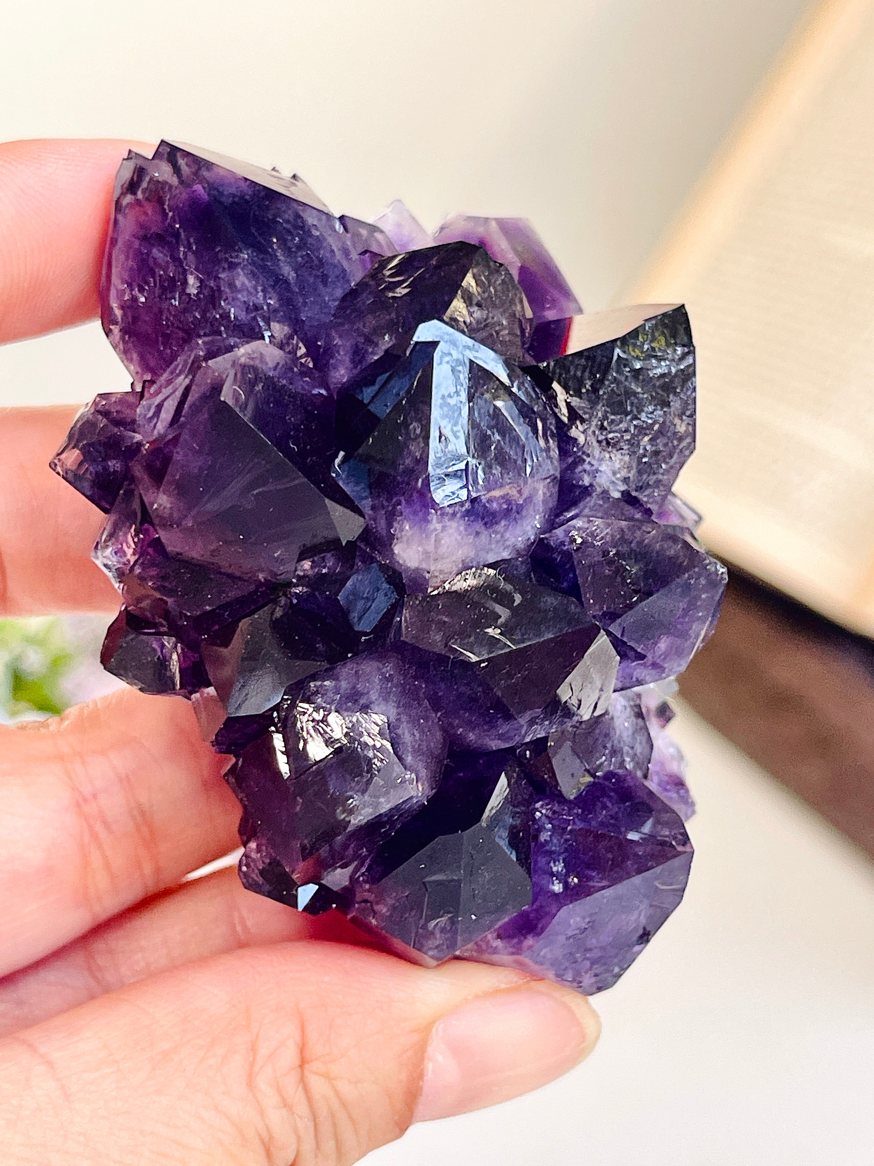 A hand holding a cluster of purple amethyst crystal points, showing the natural jagged facets and varying shades of translucent purple.