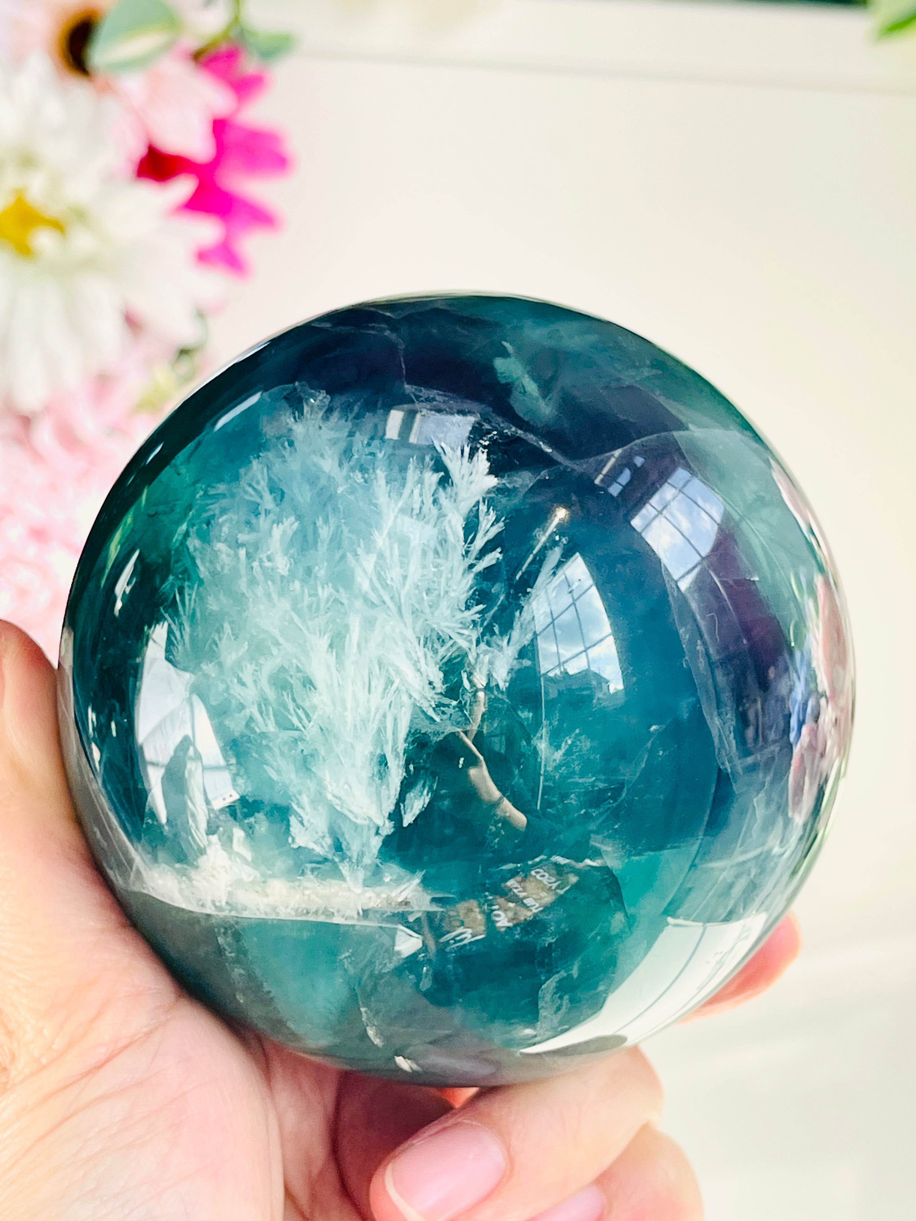 Large Green Fluorite crystal ball held in a hand with a blurred floral background