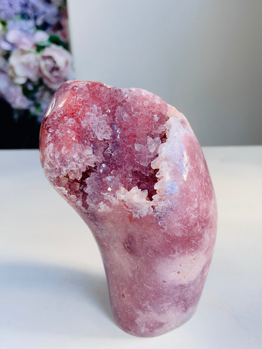 A polished pink crystal geode sculpture with a hollow interior, displayed on a white surface against a light gray background.