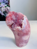 A polished pink crystal geode sculpture with a hollow interior, displayed on a white surface against a light gray background.