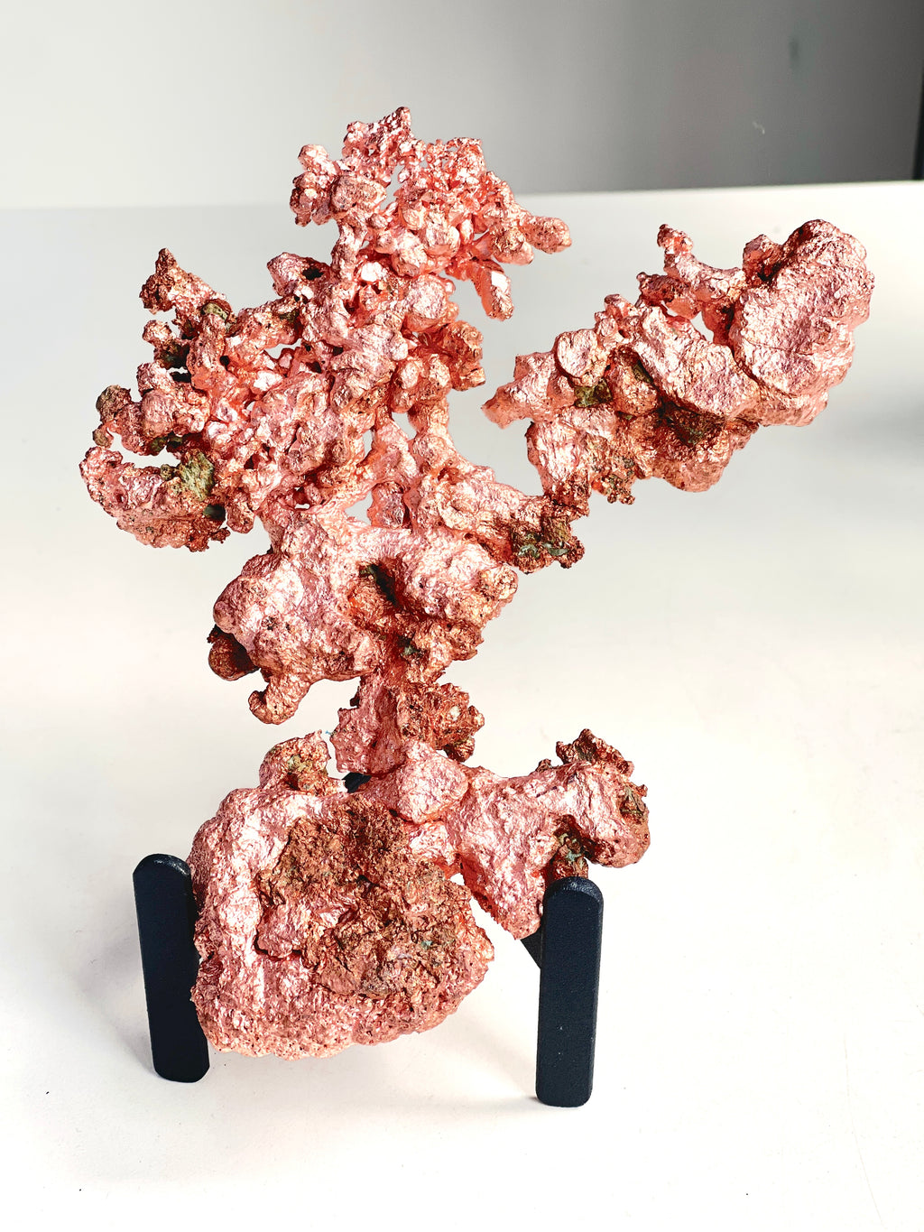 A metallic copper-colored mineral specimen or decorative rock cluster displayed on a small black stand against a plain white background.