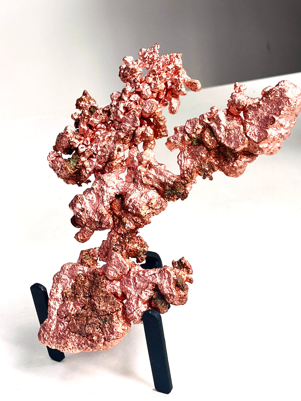 A piece of rough, textured copper mineral or metal specimen displayed on a small black stand against a plain white background.