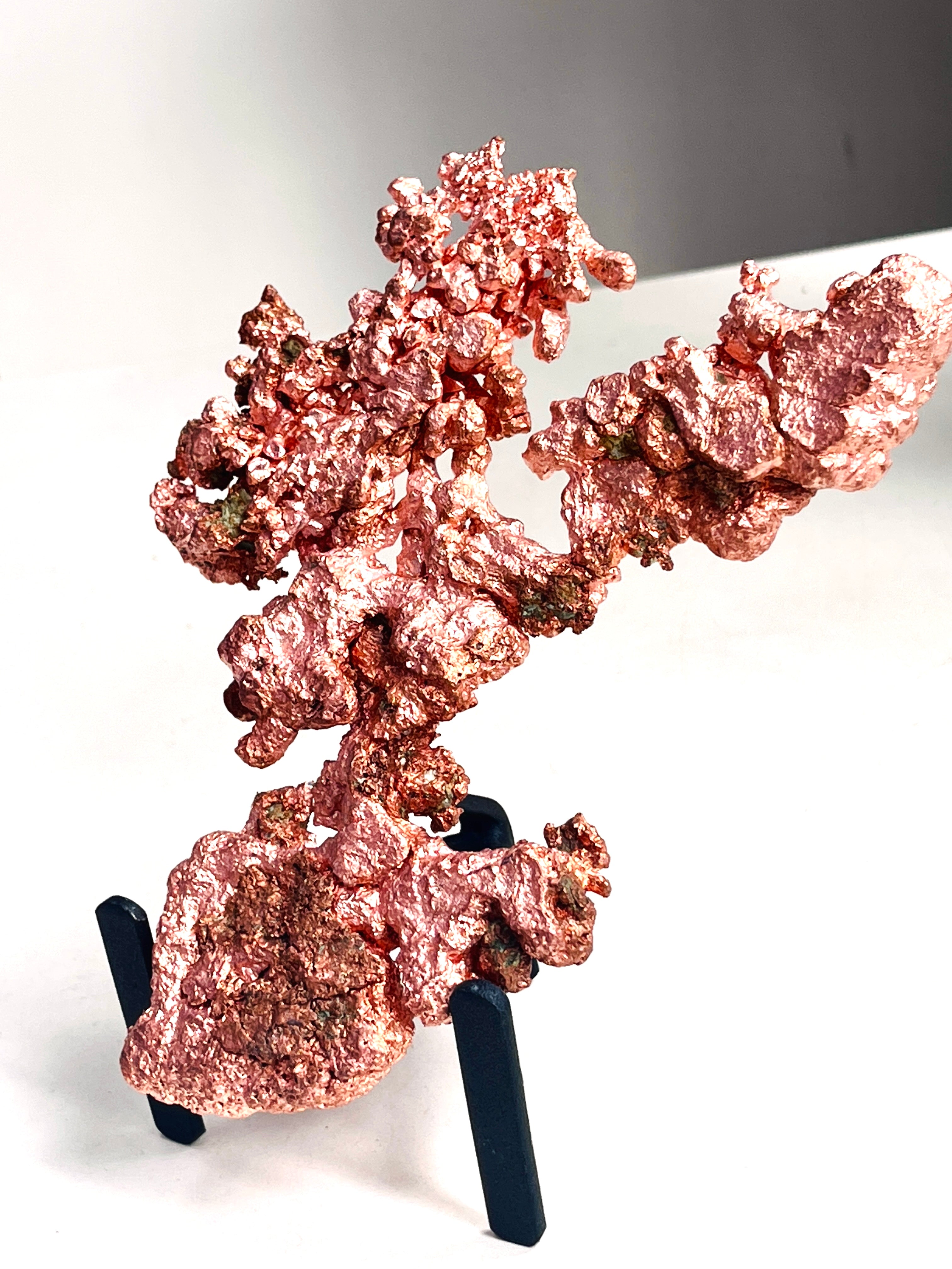 A piece of rough, textured copper mineral or metal specimen displayed on a small black stand against a plain white background.