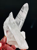 Clear crystal formation held by a hand against a black background