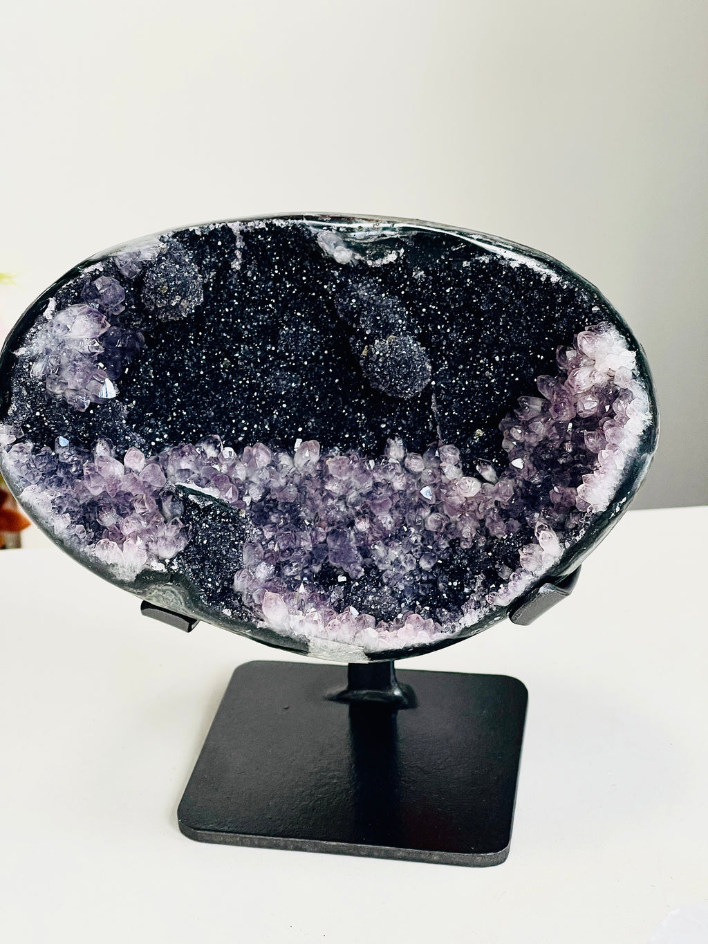 A polished amethyst geode specimen with a black cavity and purple crystal formations, displayed on a black metal stand against a plain light background.