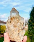 Clear crystal rock held in hand with a blurred outdoor background