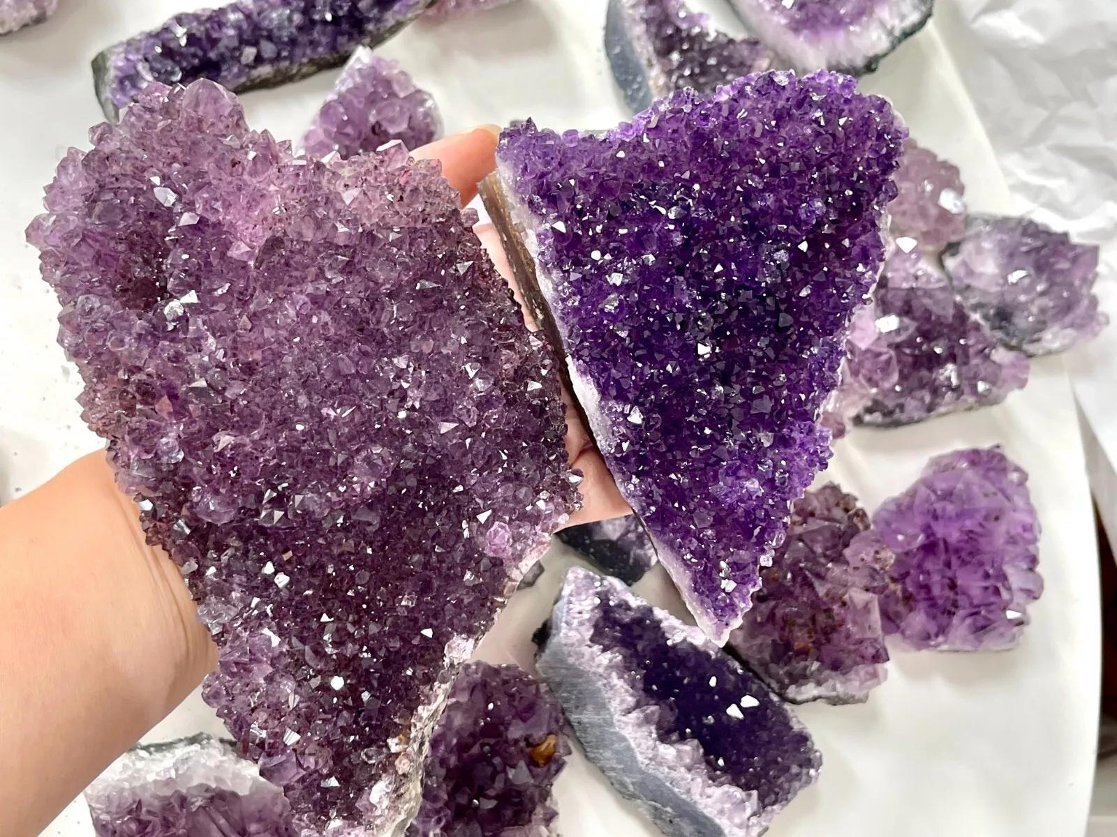 Purple crystal rock held by a hand with more crystals on a white surface