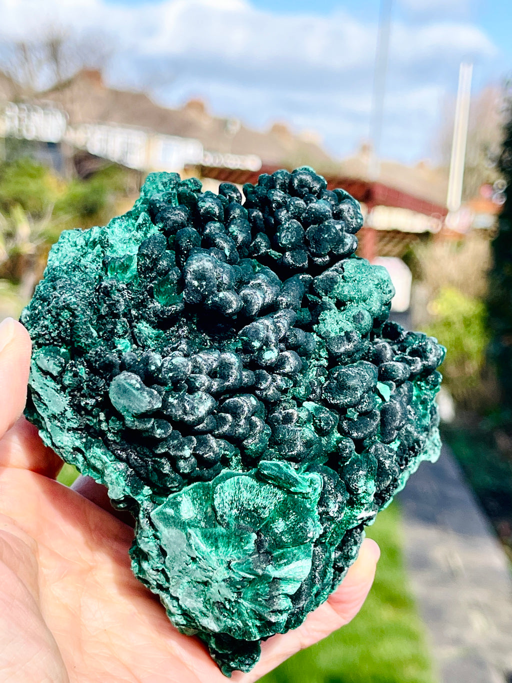 Green mineral rock held in a hand with a blurred outdoor background