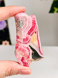 Striking pink banded Rhodochrosite stone hold in hand with neutral background, a little bit of flowers comes out from the corner of the backgroud