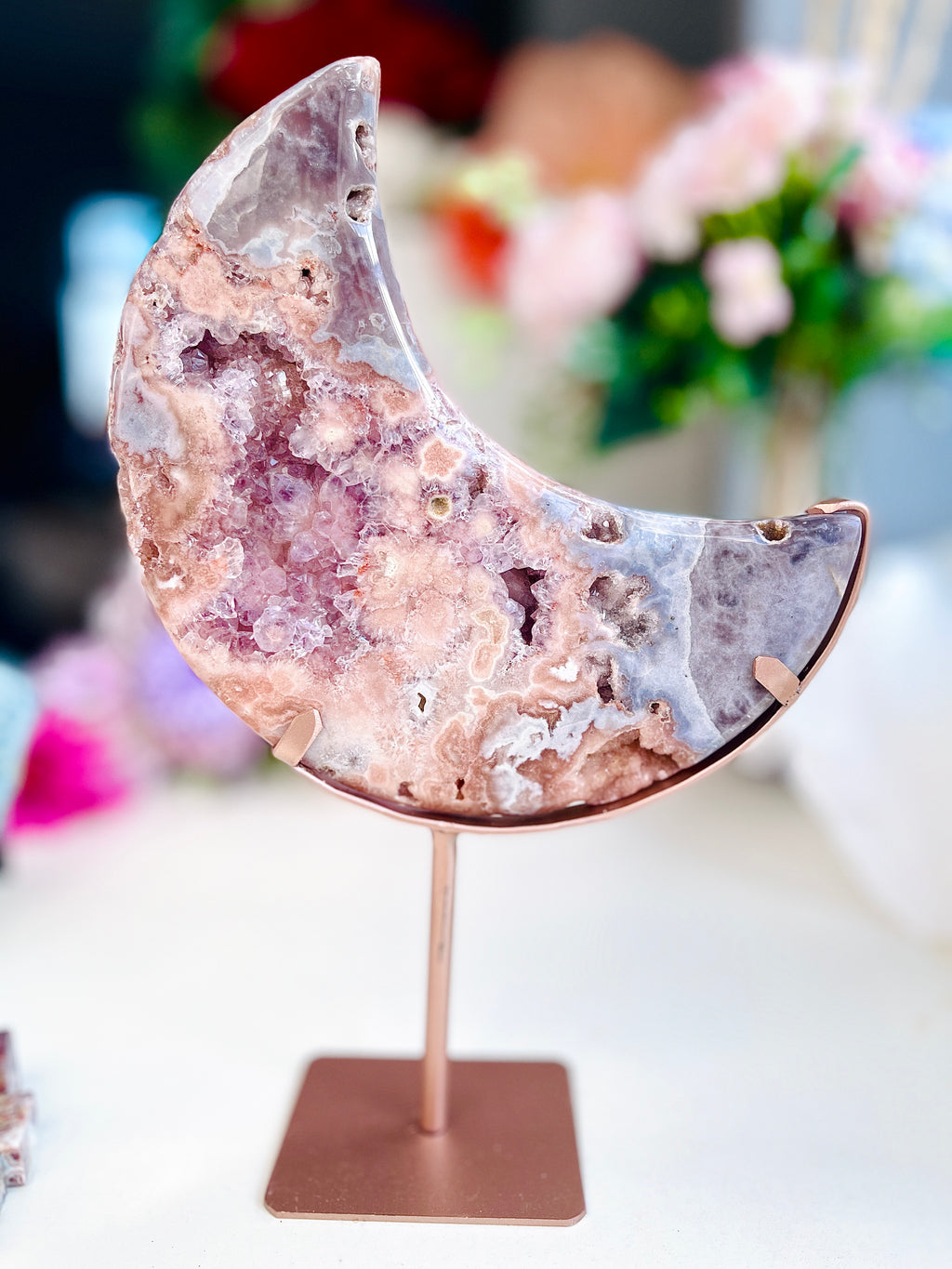 Pink Amethyst Crystal moon-shaped object on a stand with a blurred floral background