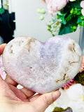 Heart-shaped pink amethyst stone held in a hand with a blurred background