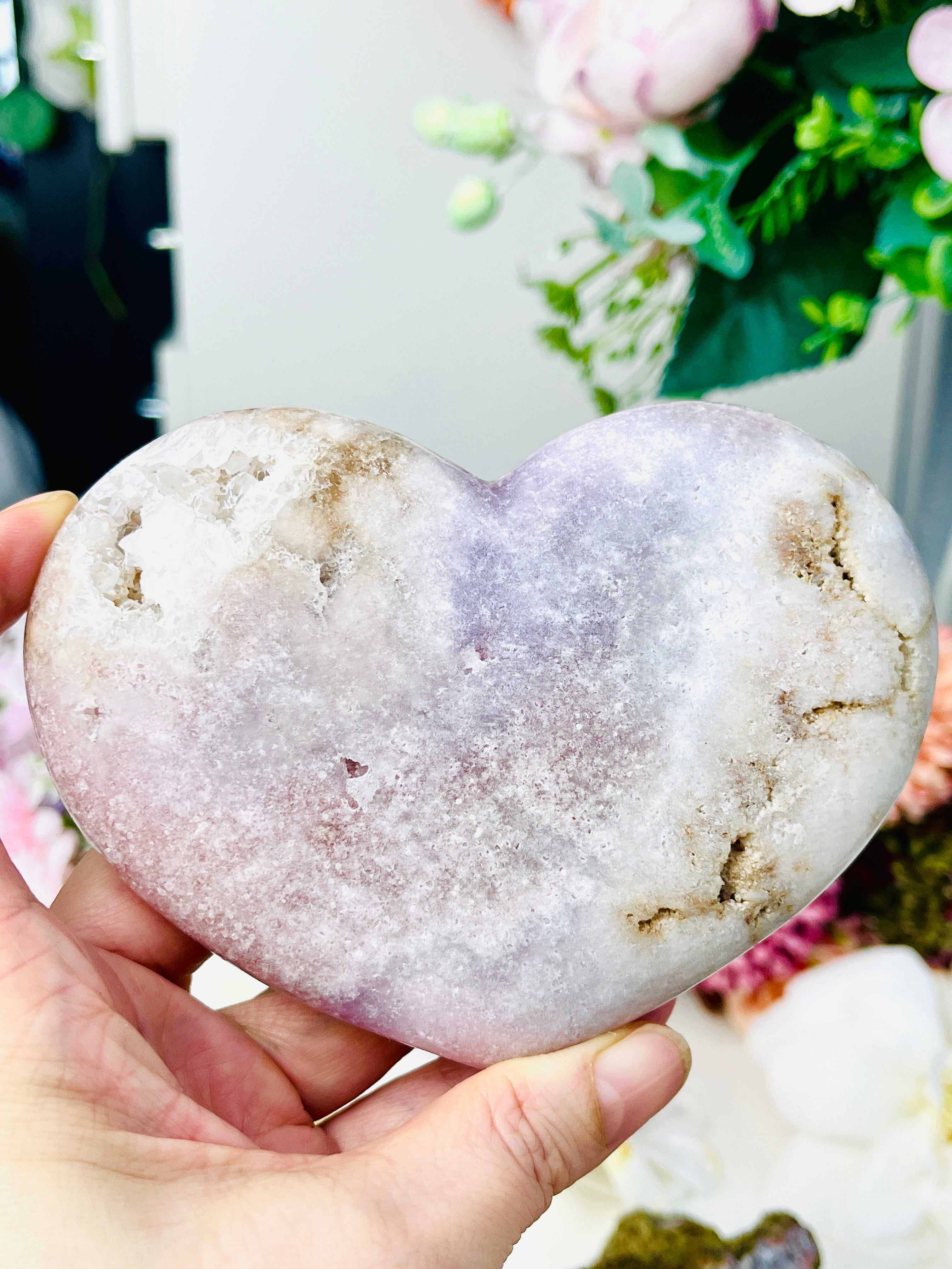 Heart-shaped pink amethyst stone held in a hand with a blurred background