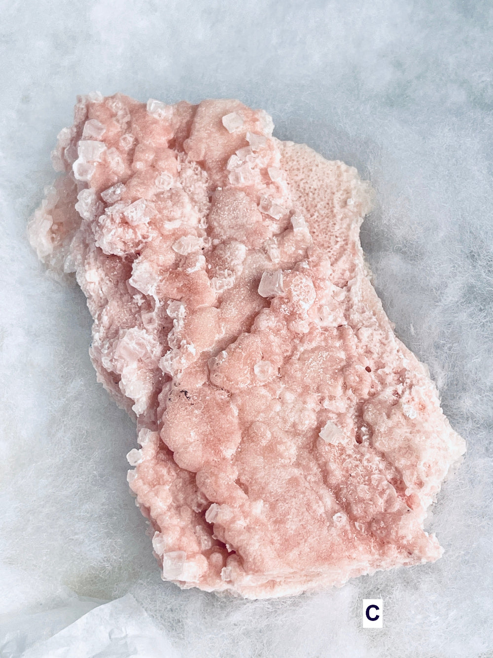 A rough, textured pink haliite mineral or crystal specimen with a bubbly, crystalline surface, photographed from above on a light gray marbled surface.