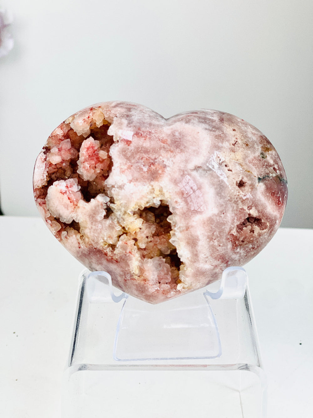 Heart-shaped pink amethyst crystal on a stand with a white background