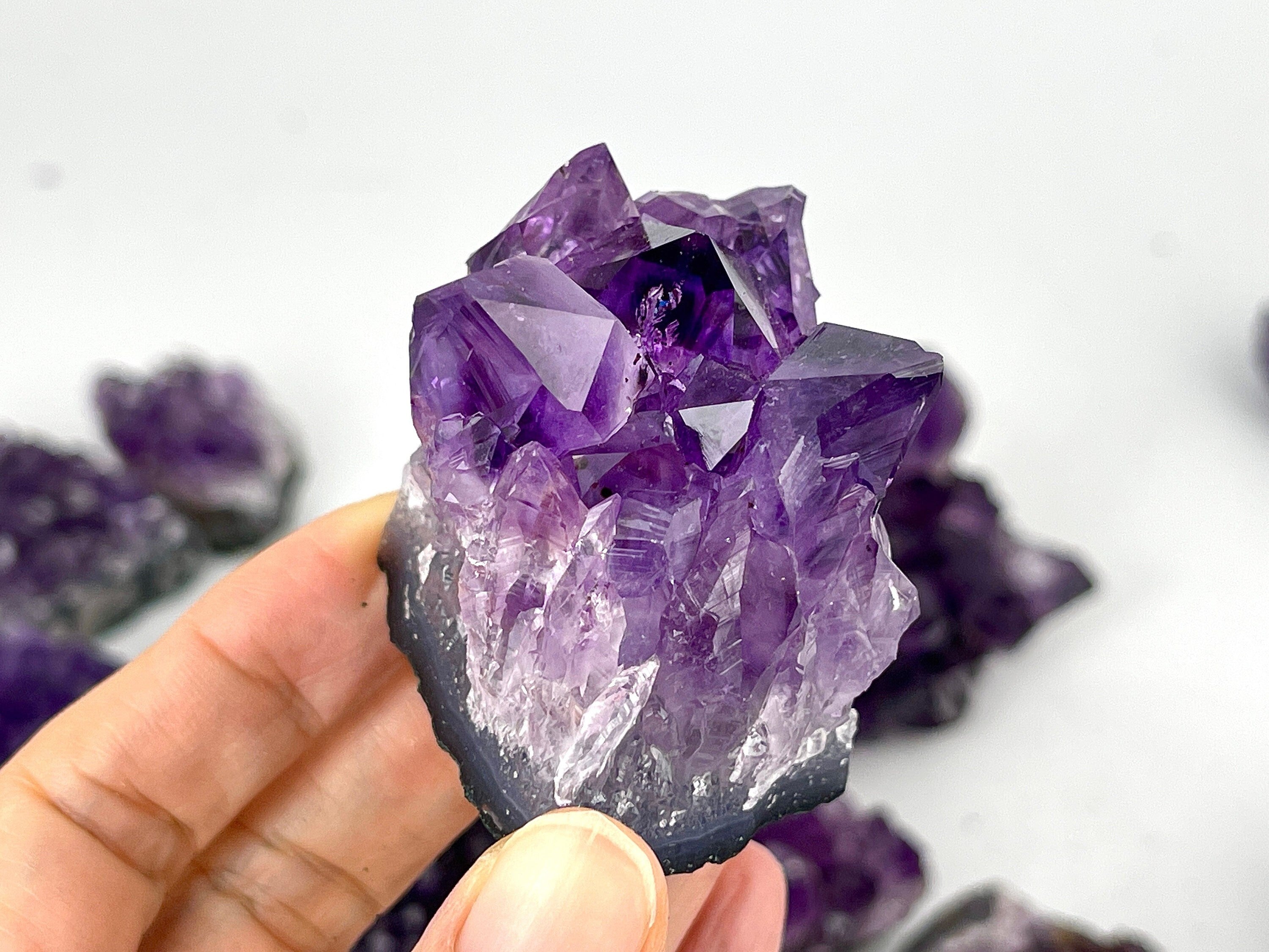 Amethyst crystal with big crystal point held by a hand against a white background
