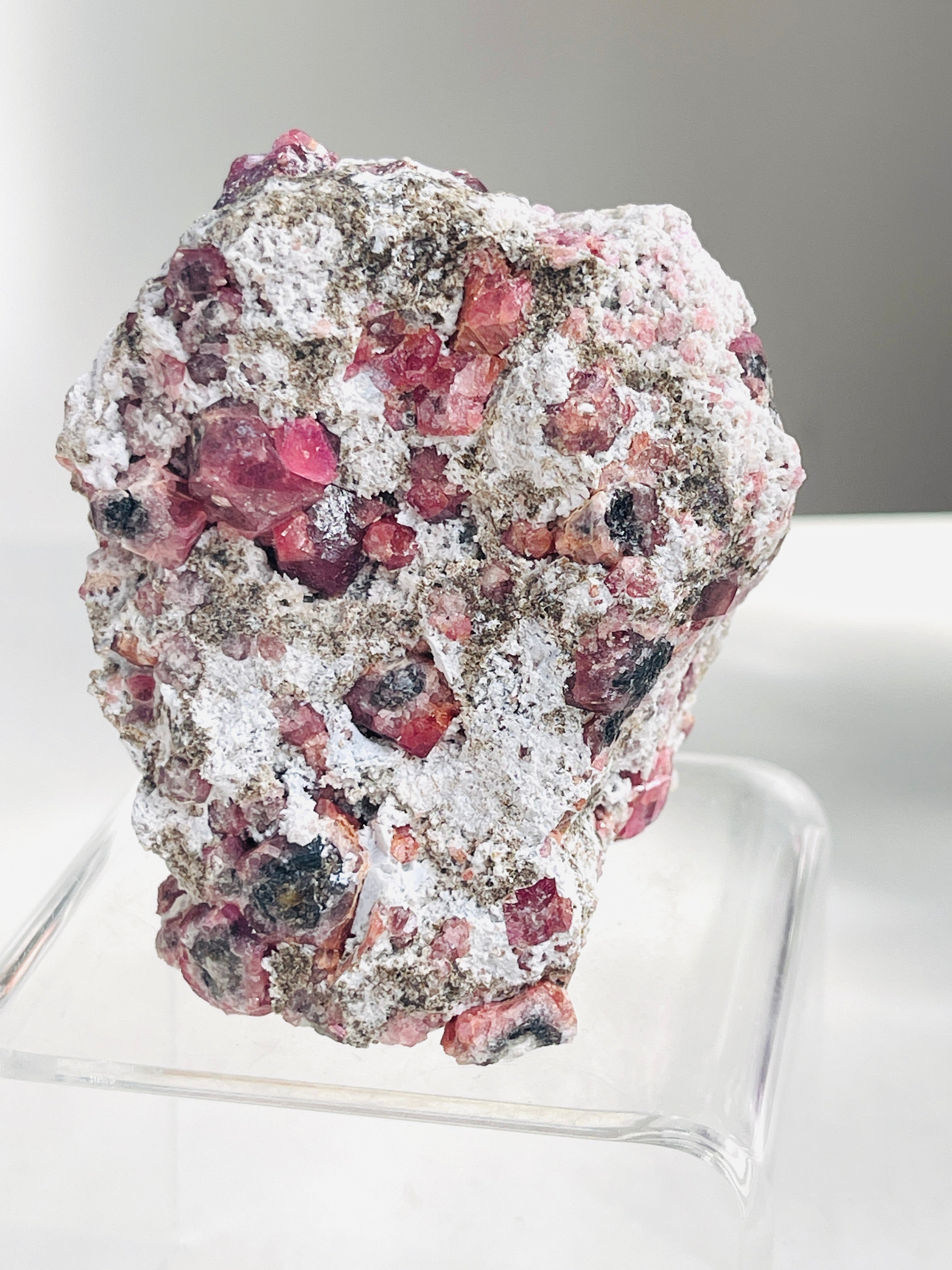 Raspberry Garnet Mineral specimen sample with pink and white crystals on a clear stand against a neutral background