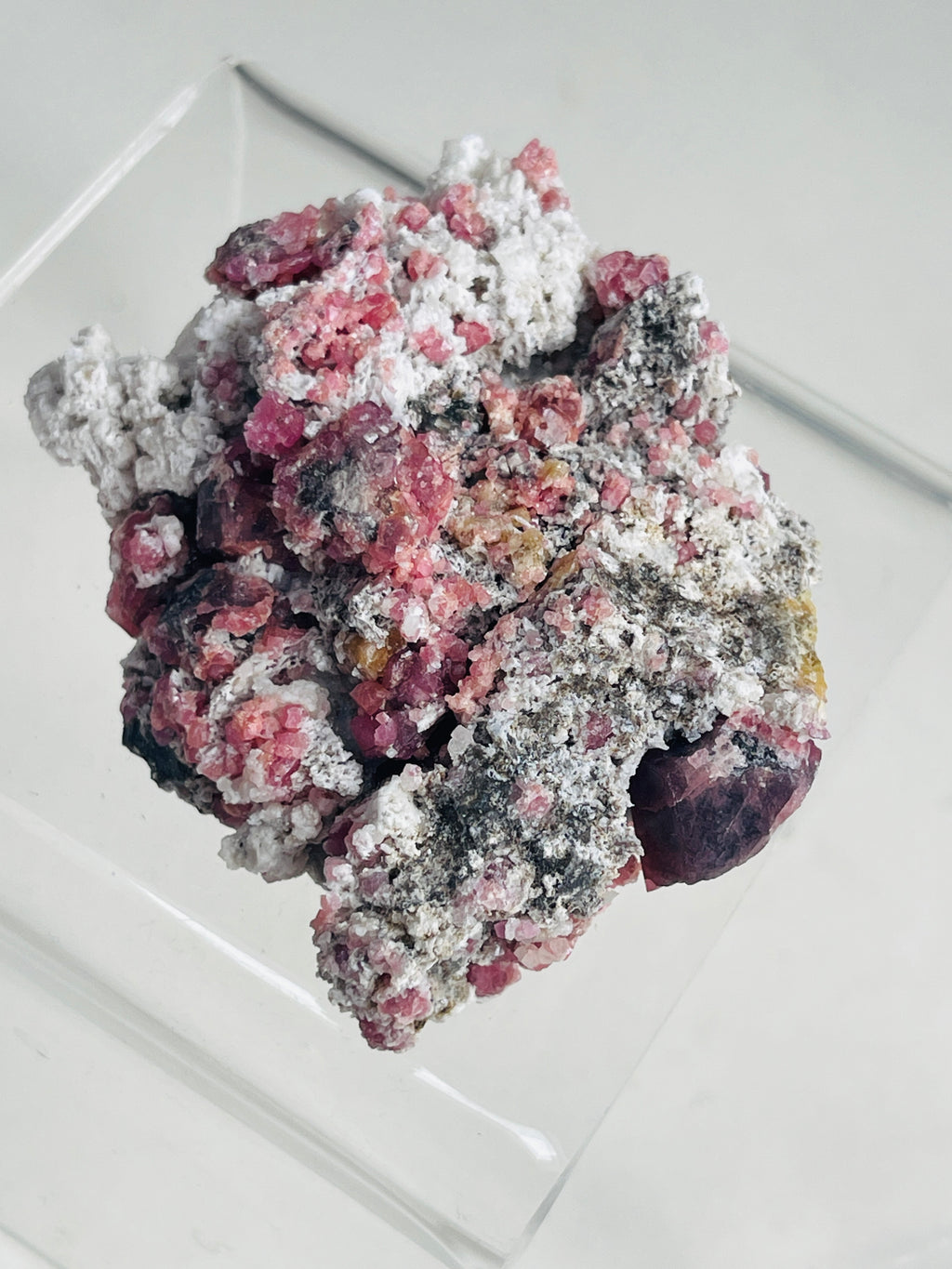 a raw raspberry pink garnet specimen on a clear stand in neutral background 