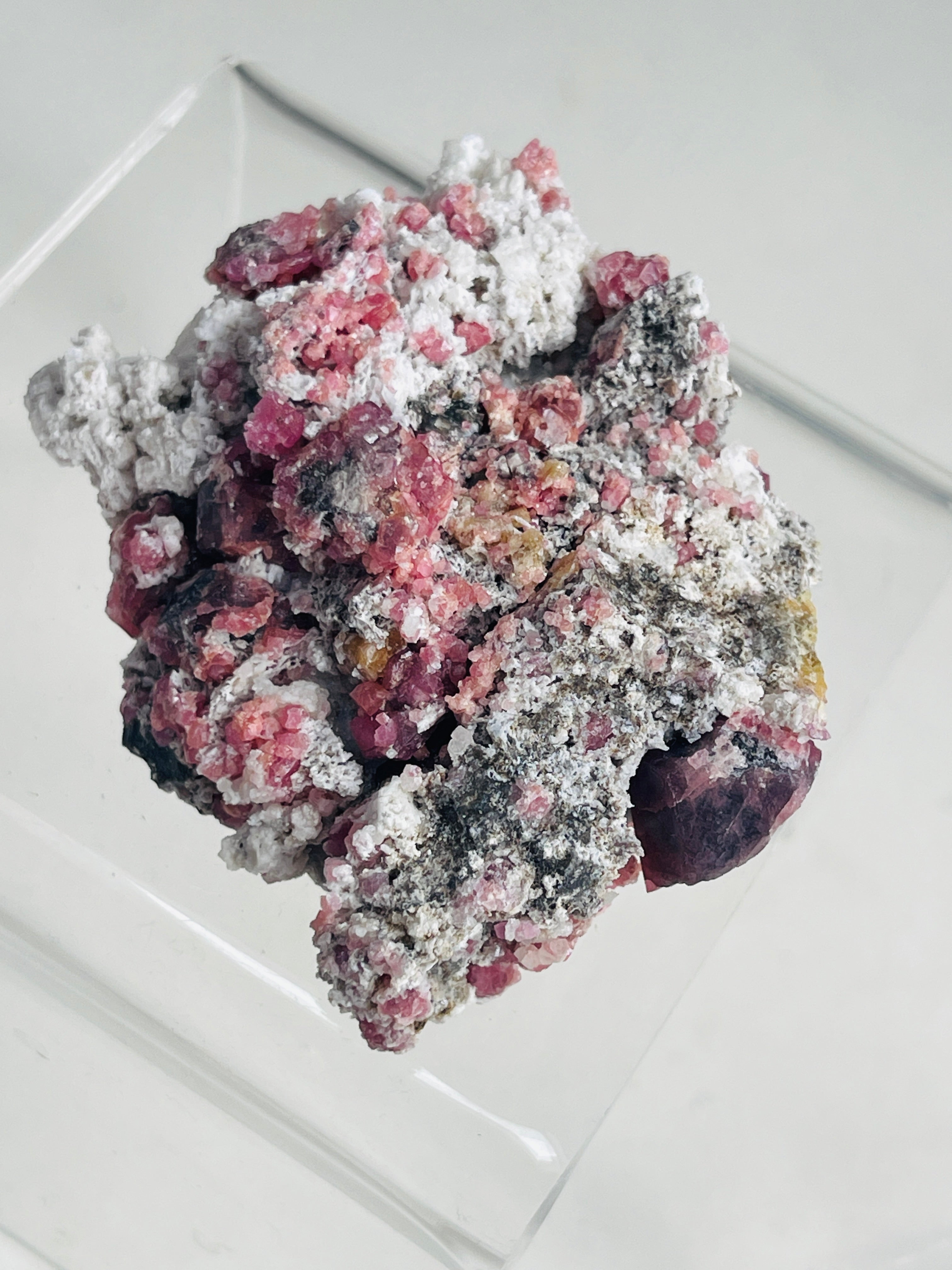 a raw raspberry pink garnet specimen on a clear stand in neutral background 