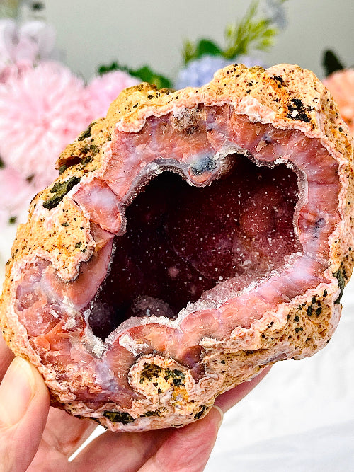 Close-up of a pink geode held in a hand with blurred flowers in the background